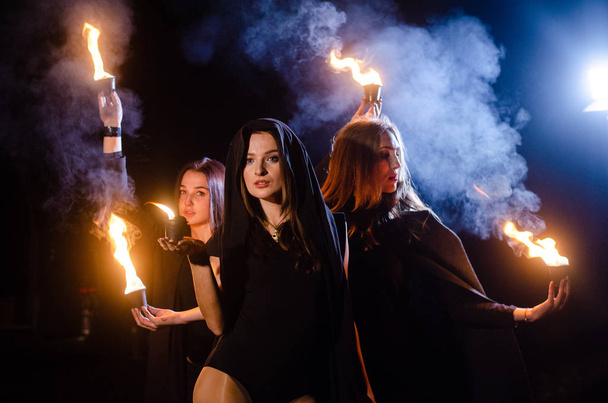 mystery young girls wearing black cloaks, witch's sabbath in the woods at the night by the bonfire - Foto, Imagem