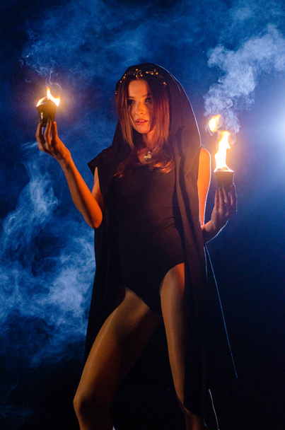 Μυστηριώδης νεαρή κοπέλα φορώντας ένα μαύρο μανδύα, Σάββατο μάγισσα στο δάσος τη νύχτα από τη φωτιά - Φωτογραφία, εικόνα
