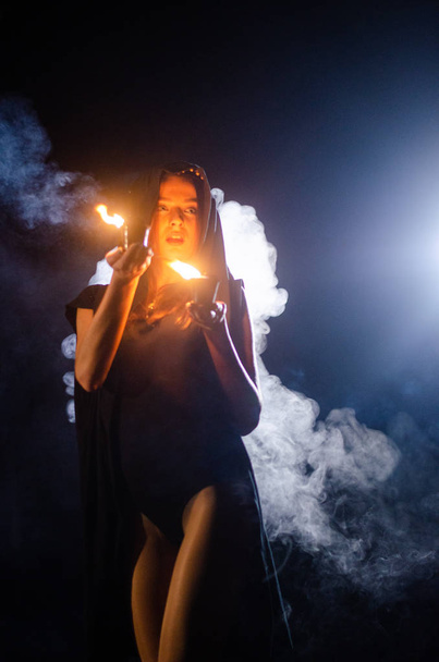 záhadná mladá dívka v černém plášti, čarodějnická sabat v lese v noci u ohně - Fotografie, Obrázek