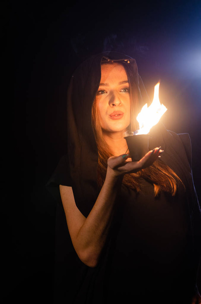 záhadná mladá dívka v černém plášti, čarodějnická sabat v lese v noci u ohně - Fotografie, Obrázek