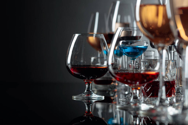 El juego de las bebidas distintas alcohólicas en los vasos por el reflejo negro
 - Foto, imagen
