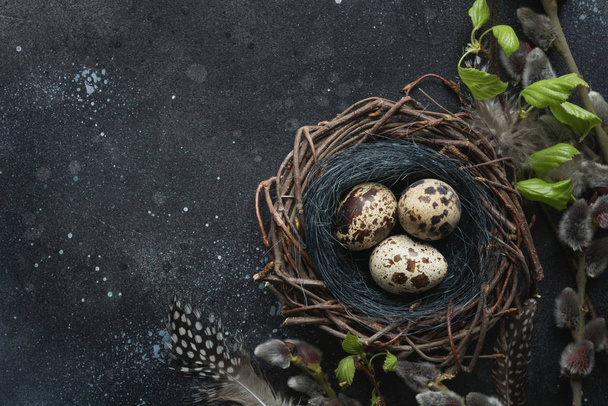 Quail eggs in nest, spring willow on dark table. Space for text. Easter composition. - Photo, Image