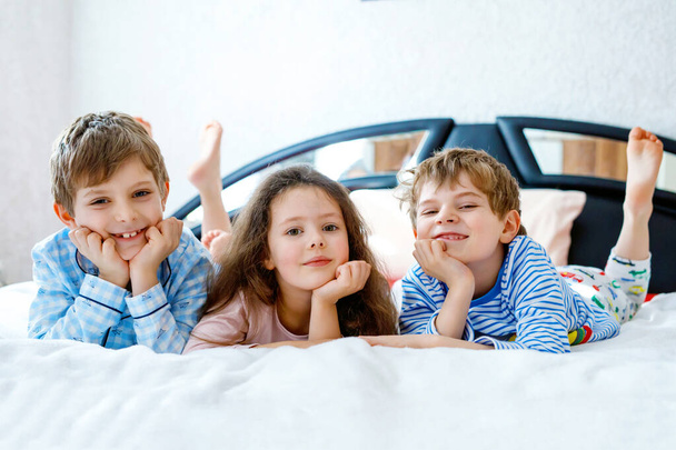 Drie gelukkige kinderen in pyjama 's die een pyjamafeest vieren. kleuterschool en school jongens en meisje hebben plezier samen - Foto, afbeelding