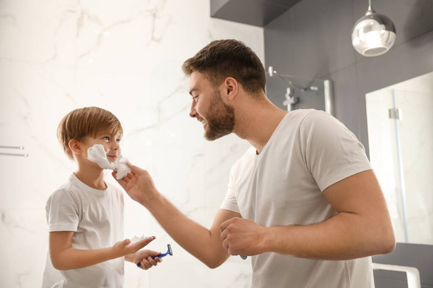 Dad applying shaving foam onto son's face in bathroom - Foto, afbeelding