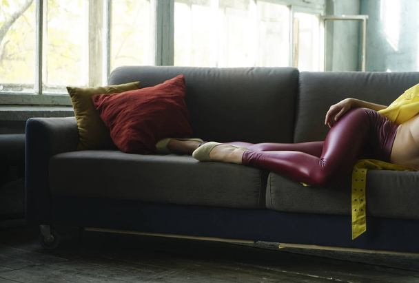 detail of woman wearing red leather  pants and  white low shoe. female lie on gray coach, sofa with two pilliows. open window. sunny day. no face. - Fotó, kép