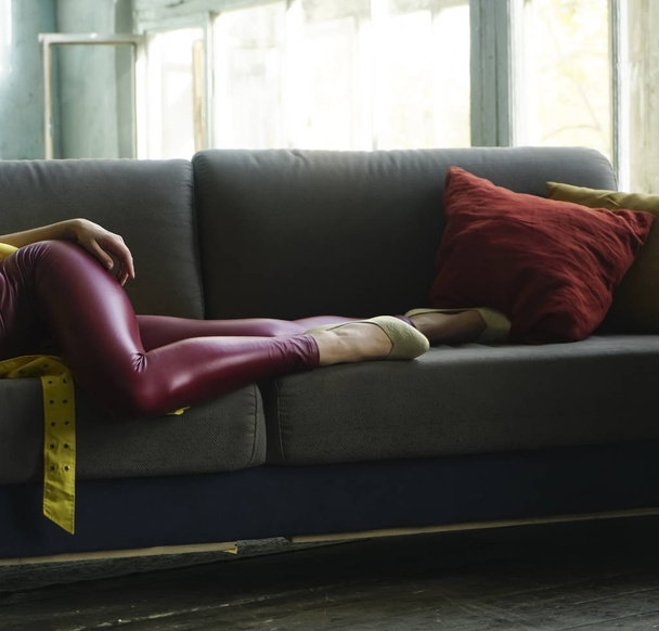 detail of woman wearing red leather  pants and  white low shoe. female lie on gray coach, sofa with two pilliows. open window. sunny day. no face. - Фото, зображення