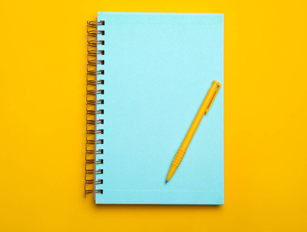 Light blue notebook and pen on yellow background, top view - Foto, Bild