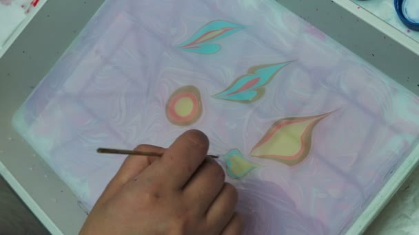 Umělkyně malující ebru techniku - umění na vodě. Kresba štětcem následovaná papírovými potisky. Barevné barvy s vlnami. Koníček, umění, kultura - Záběry, video