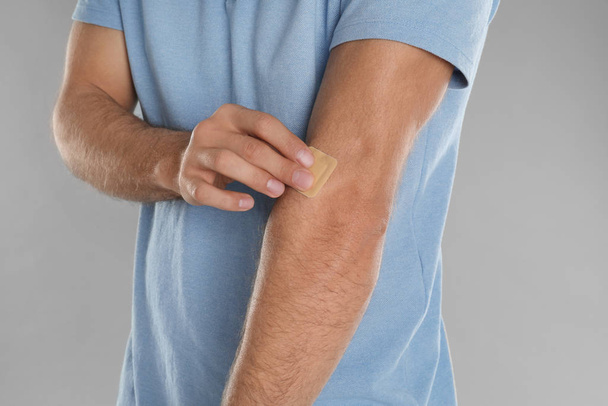 Man putting sticking plaster onto arm against light grey backgro - Foto, Imagem