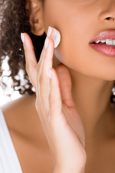 vista recortada de chica afroamericana con frenos dentales aplicando crema facial, aislado en blanco
 - Foto, Imagen