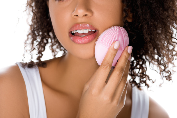 vista ritagliata della ragazza afro-americana con gli occhi chiusi utilizzando spazzola viso detergente in silicone, isolato su bianco
 - Foto, immagini