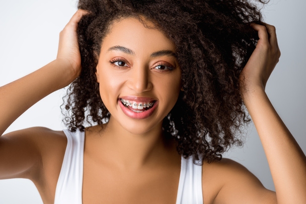 hermosa chica afroamericana positiva con frenos dentales, aislado en gris
 - Foto, Imagen