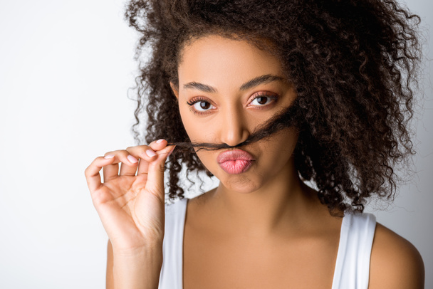 Porträt eines lustigen afrikanisch-amerikanischen Mädchens, das einen falschen Schnurrbart aus Haaren macht, isoliert auf grau - Foto, Bild