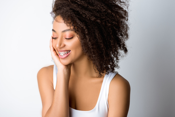 sonriente rizado africano americano chica con ortodoncia, aislado en gris
 - Foto, Imagen