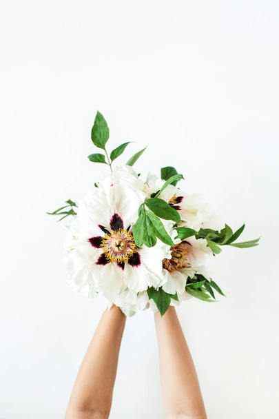 白い背景に白い牡丹の花を持つ女性の手。フラットレイアウト、トップビュー. - 写真・画像