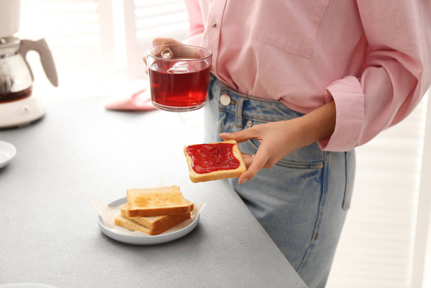 Woman having tasty breakfast with toast and raspberry tea at home, closeup. Morning routine - Фото, изображение