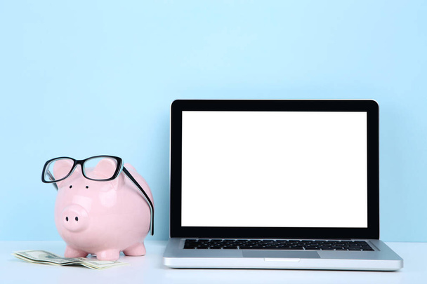 Laptop computer with piggybank and dollar banknotes on blue background - Zdjęcie, obraz