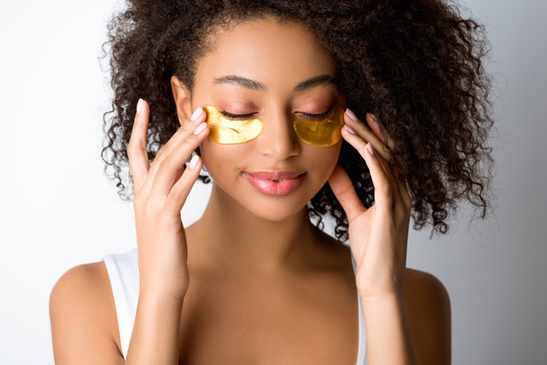 привлекательная улыбающаяся африканская американка с золотыми повязками на глазу, изолированная на сером
 - Фото, изображение