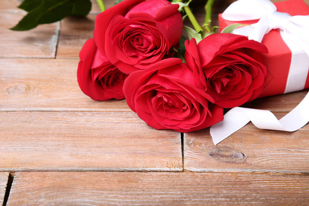 Bouquet of red roses with gift box on brown wooden table - Valokuva, kuva