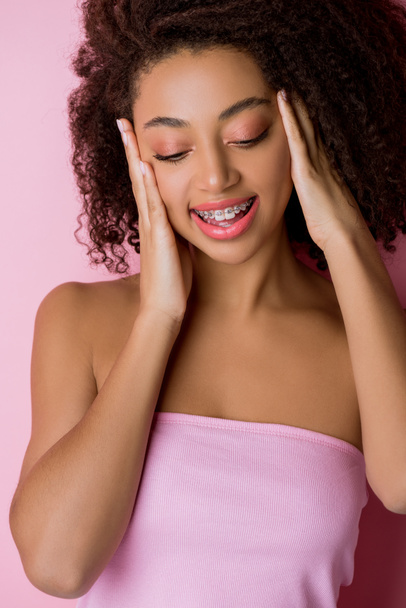 улыбающаяся африканская американка с зубными скобками, изолированная на розовом
 - Фото, изображение
