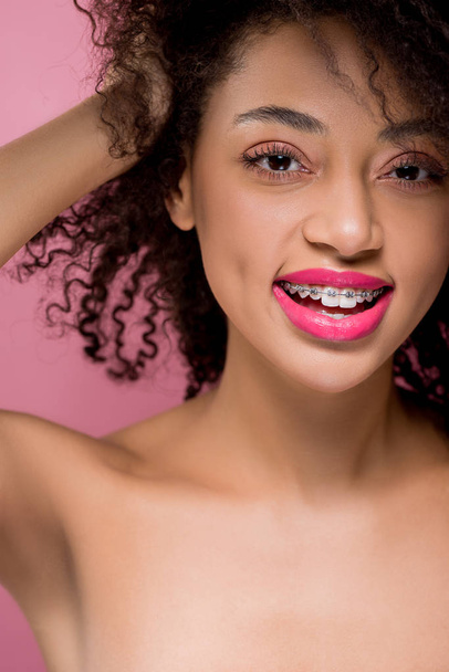 feliz positivo desnudo afroamericano chica con frenos dentales, aislado en rosa
 - Foto, Imagen