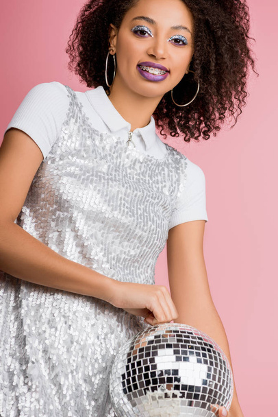 happy young african american woman in paillettes dress holding disco ball, isolated on pink  - Zdjęcie, obraz