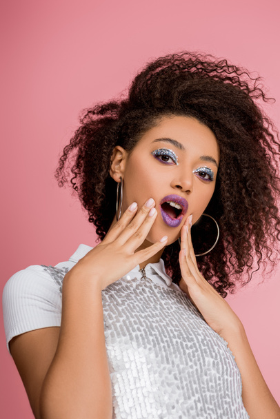 shocked african american girl with silver glitter eyeshadows and purple lips wearing paillettes dress, isolated on pink - Foto, Bild