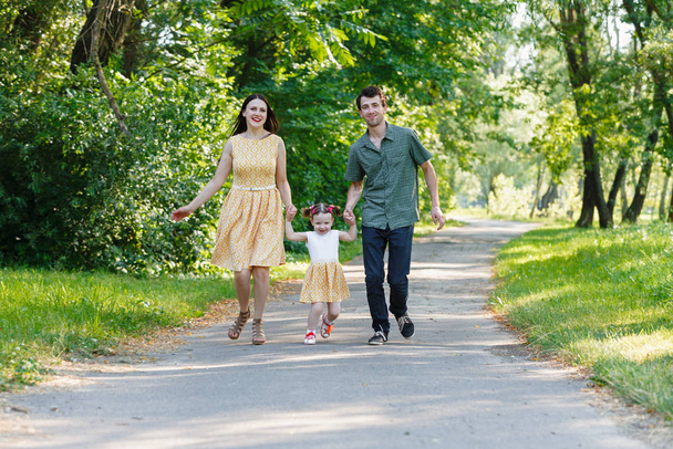 glückliche Familie läuft auf dem Weg Händchen haltend und verbringt Zeit im schönen grünen Park. Frau schwanger. - Foto, Bild