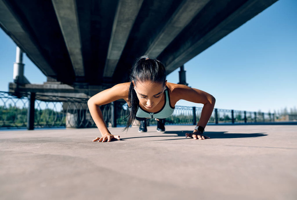 Young athletic woman doing push ups outdoors in urban city background. Sport activity                         - Zdjęcie, obraz