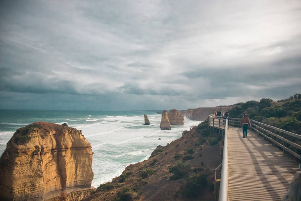 Group of people walking on a boardwalk near the sea with a lot of rock formations - Foto, Imagen