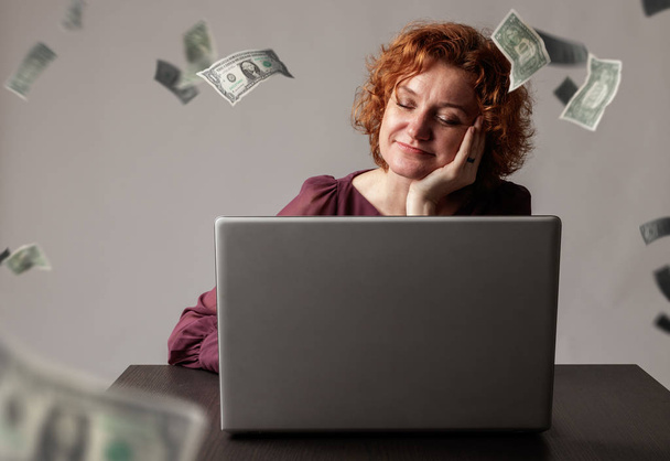 Red-haired woman with laptop. Red-haired woman and falling dolla - Φωτογραφία, εικόνα