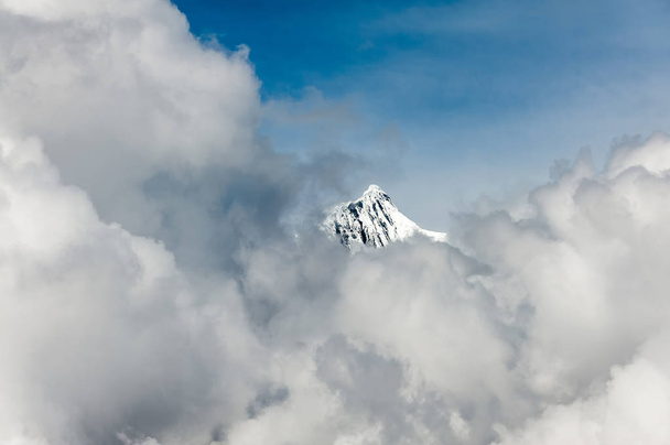 Dalle nuvole emerge la vetta innevata di Kawagarbo (Khawa Karpo, Kawadgarbo, Khawakarpo, Moirig Kawagarbo, Kawa Karpo o Kha-Kar-Po). 6.740 mt in vetta. Montagna sacra nel mondo tibetano. - Foto, immagini