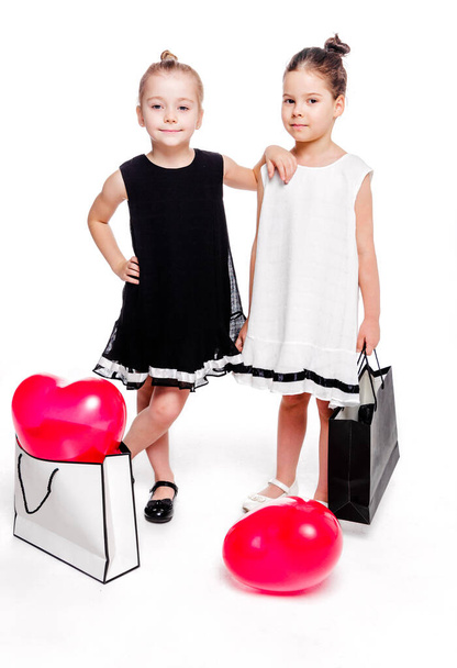 エレガントなドレスを着た2人の女の子は、ハート型の風船を内側にした大きな袋の横にいます - 写真・画像