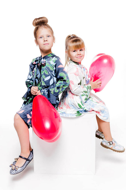 2 meninas com vestidos elegantes sentar com grandes sacos com balões em forma de coração dentro
 - Foto, Imagem
