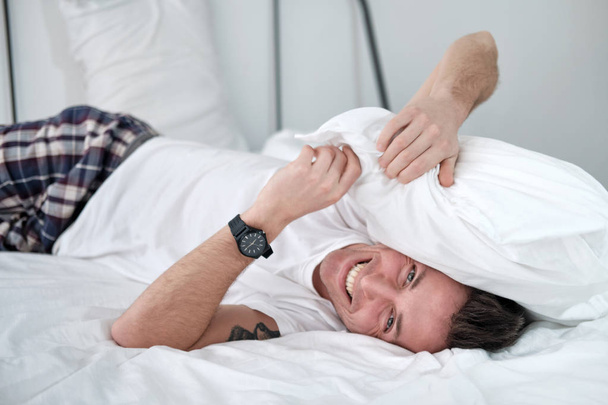 Jeune homme dans la chemise blanche couché sur un lit avec du linge blanc et couvre sa tête avec une lueur
 - Photo, image