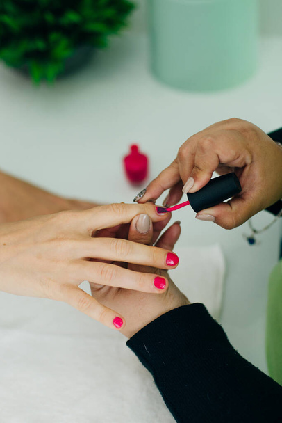 Manicurist applying pink nail varnish to the fingernails of a lady client in a spa or beauty salon - Photo, Image