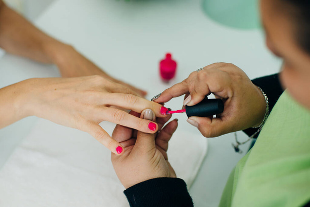 Manicure aplicando verniz de unhas rosa nas unhas de uma senhora cliente em um spa ou salão de beleza - Foto, Imagem