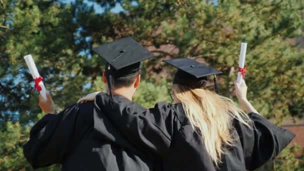 Vista trasera de los graduados se felicitan mutuamente por graduarse de la universidad, abrazos
 - Imágenes, Vídeo