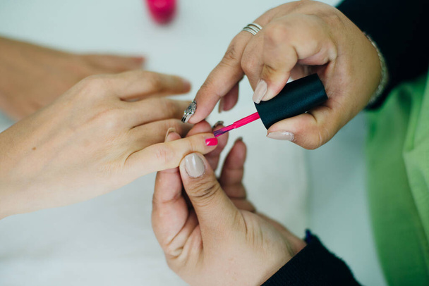Manikiurzystka nakładająca różowy lakier do paznokci na paznokcie klientki w spa lub salonie piękności - Zdjęcie, obraz