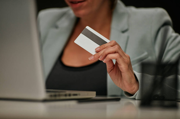 Jovem mulher de negócios caucasiana sentada em seu escritório e usando cartão de crédito para pagar assinatura de software licenciado
. - Foto, Imagem