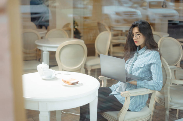 Portrait of a young female freelancer using laptop computer for distance job while sitting in modern coffee shop interior, smart woman working on net-book during morning breakfast in cafe bar - Фото, зображення