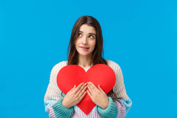 Dreamy lovely and shy, thoughtful attractive woman want give valentines day heart cardboard to express sympathy, confess love and affection, dreamy looking up, biting lip tempting, blue background - Photo, Image