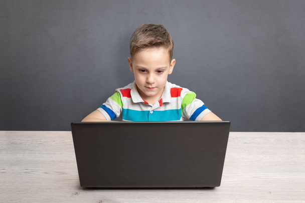 Chłopak pracuje na laptopie i biurku. Koncepcja korzystania z komputerów do gier i uczenia się. Z przodu. Czysta ściana z miejscem na tekst w tle - Zdjęcie, obraz