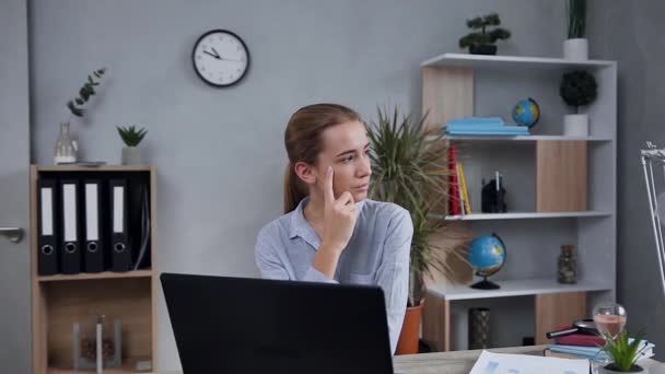 Thinking good-looking young blond lady in casual clothes sitting at the table while working at the computer and looking away - Video