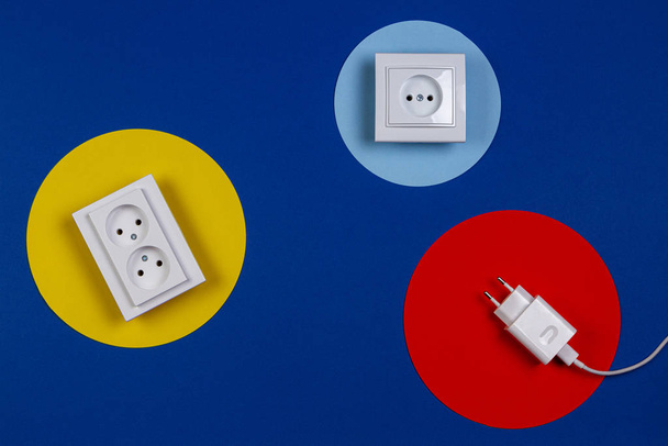 Câble blanc et prises électriques sur fond géométrique jaune rouge bleu marine
 - Photo, image
