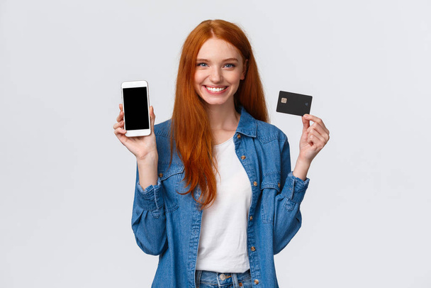 Vyötärö-up muotokuva luottavainen nainen punaiset pitkät hiukset, siniset silmät, jolla luottokortti ja näytetään älypuhelin näyttö, helppo pankkipalvelu, maksu laskut internet, hymyillen tyytyväinen - Valokuva, kuva