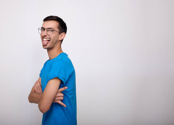 A cheerful young man shows his tongue on a white background. - Fotoğraf, Görsel