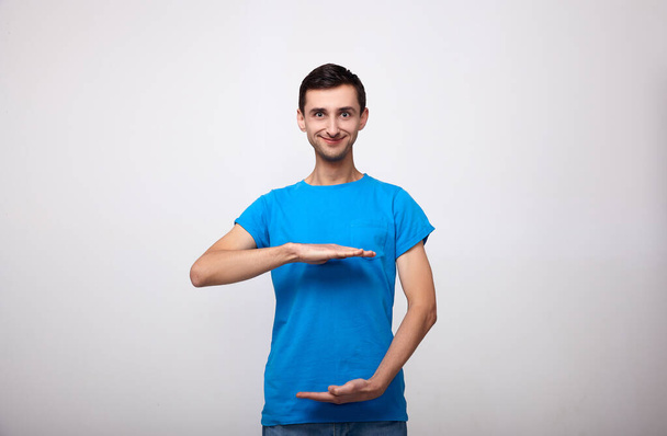 A c cute man in a blue T-shirt shows the size of something. - Photo, Image