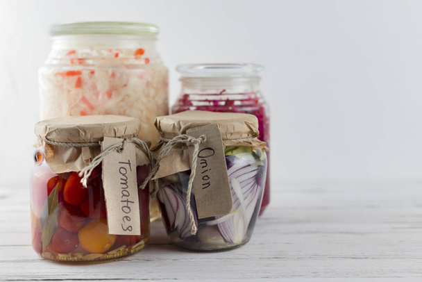jarros de vidro de repolho branco fermentado, pepinos, tomate, cebolas. legumes em um fundo leve. a fermentação é uma fonte de probiótico
 - Foto, Imagem