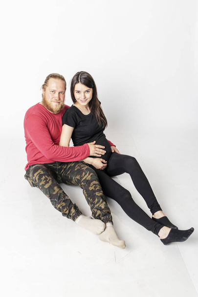Caucasian man with a beard in a red sweater hugs a pregnant Caucasian girl - Foto, afbeelding